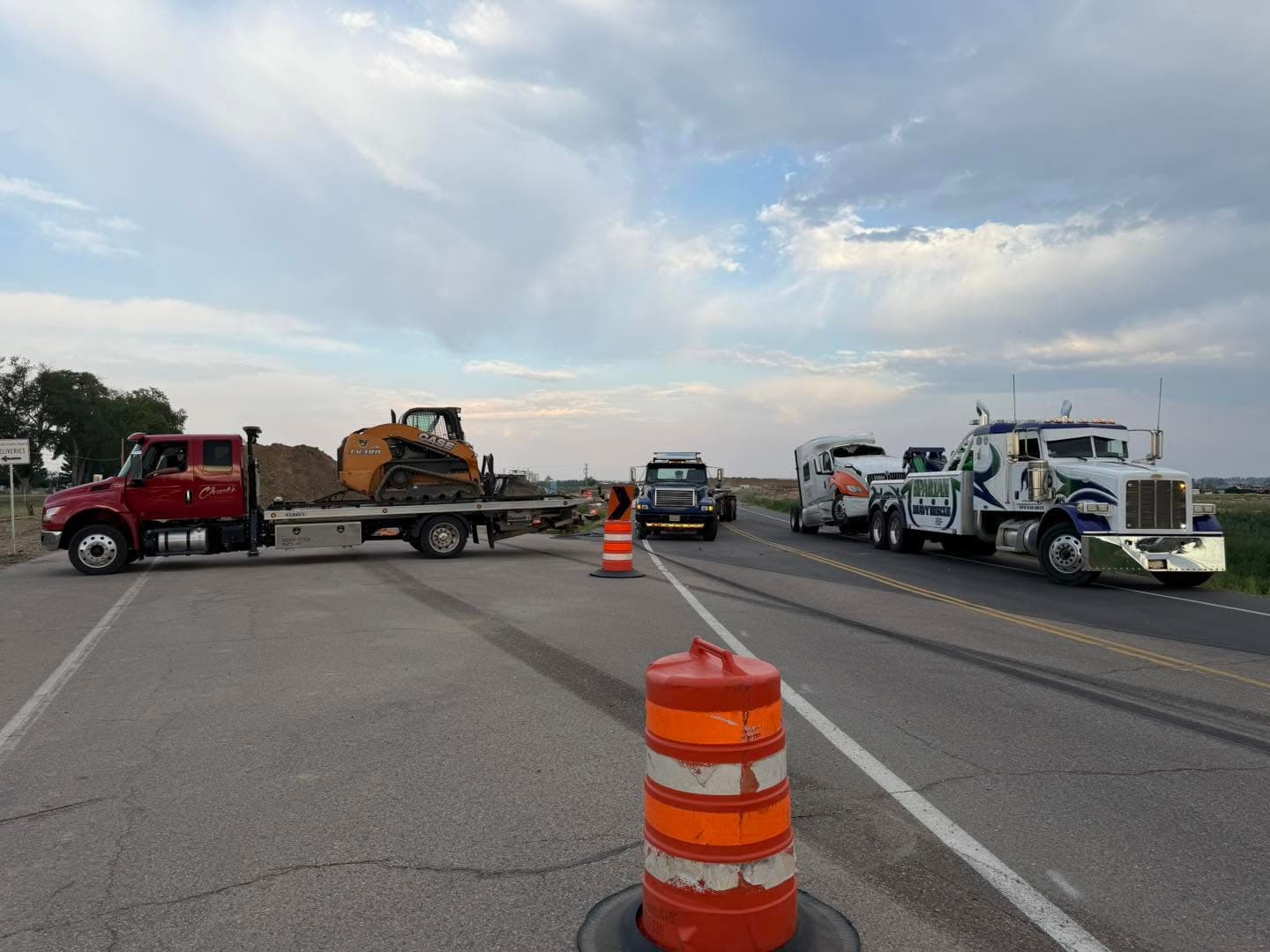 Multiple tow trucks and equipment staged on a highway with cones