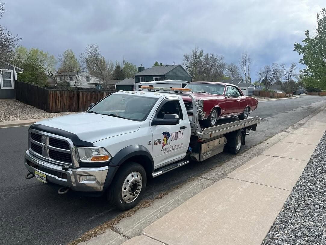 Flatbed carrying a red vintage coupe through a residential street