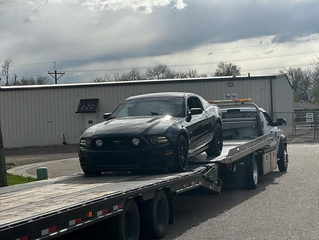 Flatbed carrying a black Mustang past an industrial building